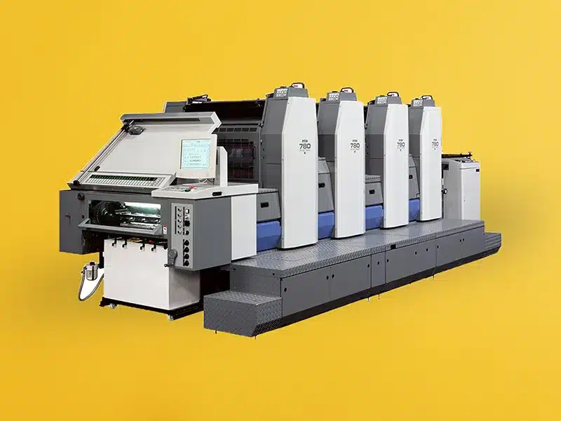 Große industrielle Offsetdruckmaschine mit mehreren Druckwerken vor gelbem Hintergrund.