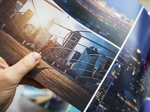 Eine Hand hält eine aufgeschlagene Broschüre mit Fotos von modernen Stadtlandschaften und Hochhäusern bei Tag und bei Nacht.