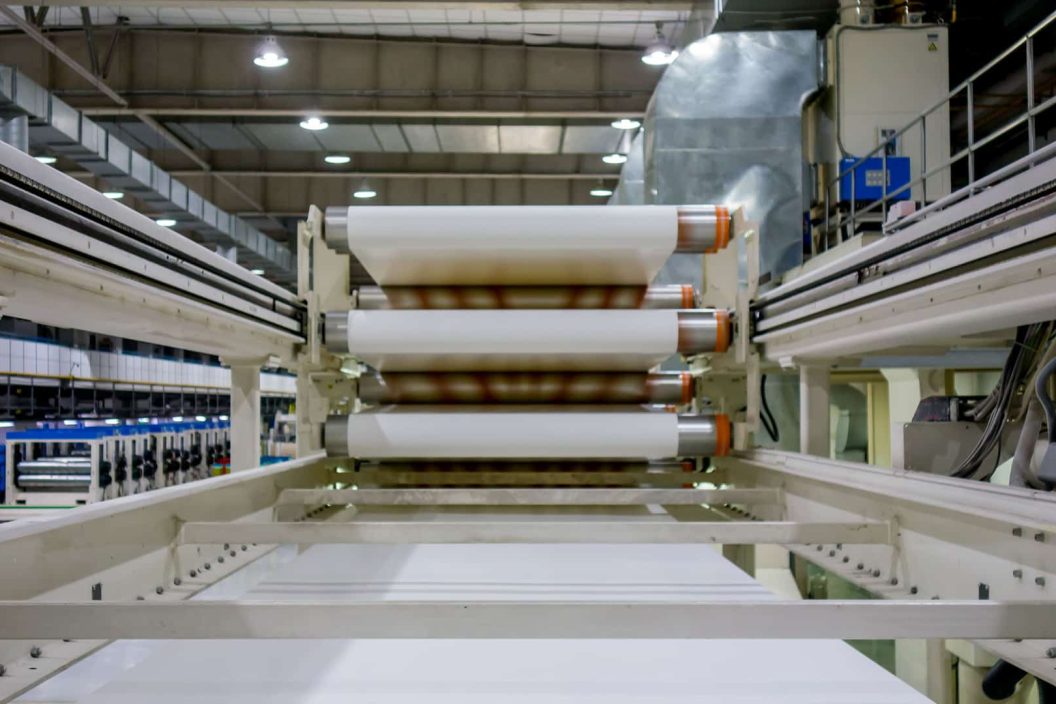 Industrielle Papierverarbeitungsmaschine mit mehreren großen Papierrollen in einer modernen Fabrikumgebung.